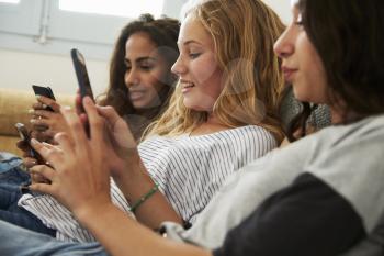 Three teenage girls using smartphones at home, close up