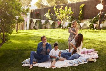Parents Blowing Bubbles With Children On Blanket In Garden