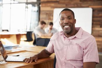 Smiling young black man in creative office looking to camera
