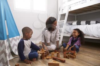 Mother And Children Playing With Building Blocks In Bedroom