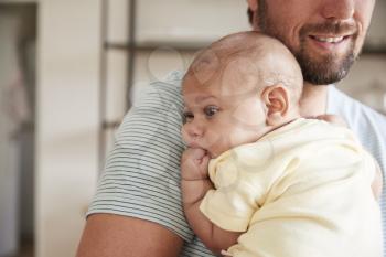 Close Up Of Father Comforting Newborn Baby Son In Nursery