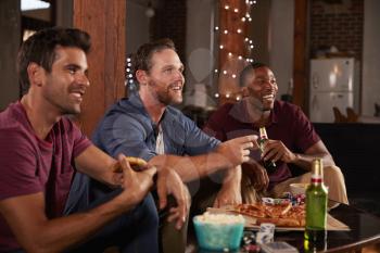 Three male friends hang out watching TV and eating pizza