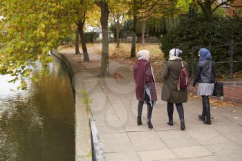 British Muslim Female Friends Walking By River In City