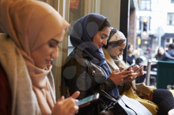 Group Of British Muslim Women Texting Outside Coffee Shop