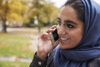 British Muslim Woman Using Mobile Phone In Park