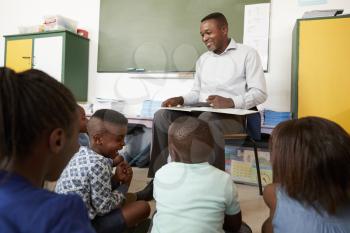 Elementary school teacher reading to kids sitting on floor