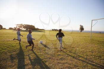 Three elementary school kids playing football in a field