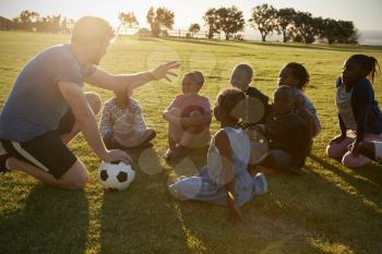 Elementary school kids and teacher sitting with ball in field