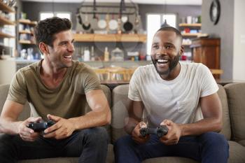 Two Male Friends Sitting On Sofa In Lounge Playing Video Game