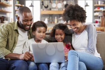 Family Sitting On Sofa In Open Plan Lounge Using Laptop