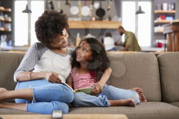 Mother And Daughter Sit On Sofa In Lounge Reading Book Together