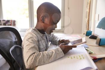 Boy In Bedroom Using Digital Tablet To Do Homework