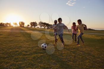 Four children chasing a ball during a game in a field