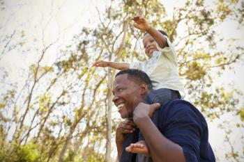 Father Carrying Son On Shoulders As They Walk In Park