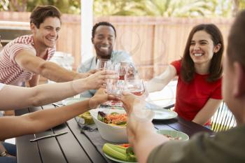 Adult friends sitting at a table outdoors making a toast