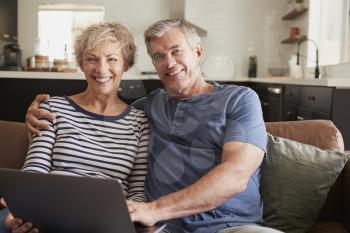 Senior couple sitting on couch use laptop, smiling to camera