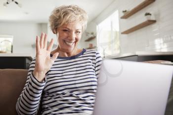 Senior woman video calling on a laptop, waving at screen