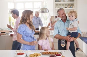 Multi-Generation Family And Friends Gathering In Kitchen For Celebration Party