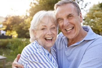 Portrait Of Loving Senior Couple Hugging Outdoors In Summer Park Against Flaring Sun