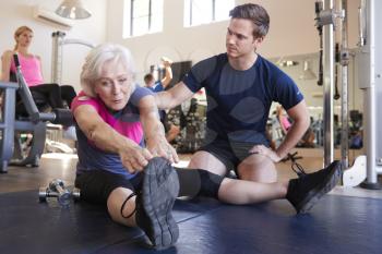 Senior Woman Exercising In Gym Being Encouraged By Personal Trainer