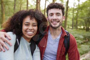 A young adult mixed race couple smiling to camera during a hike in a forest, portrait