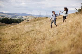 Mixed race young adult couple holding hands while walking walking down a hill during a mountain hike