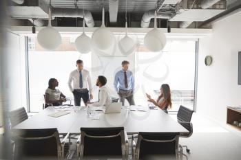Businessmen And Businesswomen Meeting Around Table In Modern Boardroom