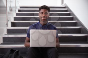 Portrait Of Male High School Student Sitting On Staircase And Using Laptop