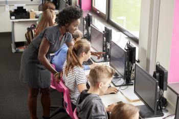 Teacher Helping Female Pupil Line Of High School Students Working at Screens In Computer Class