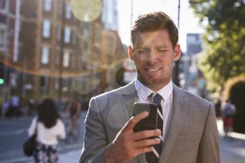 Businessman Walking To Work In City Looking At Mobile Phone