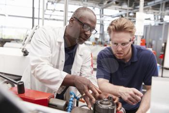 Engineer advising a male apprentice in a factory, close up