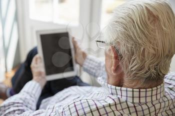 Senior man using tablet computer at home, over shoulder view