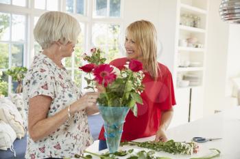 Senior woman and adult daughter arranging flowers at home