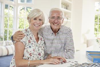 Senior couple doing a jigsaw puzzle at home, smiling to camera