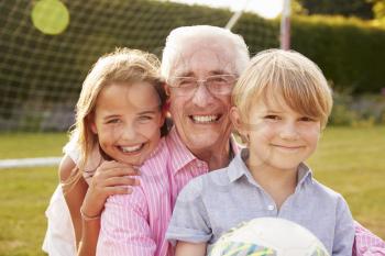 Senior man and grandchildren holding ball smiling to camera