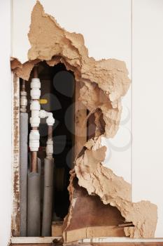Damaged wall exposing burst water pipes after flood, vertical