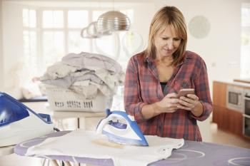 Middle aged woman distracted by phone while ironing t shirt