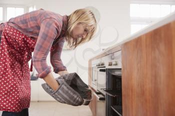 Middle aged woman bending down to take food out of the oven