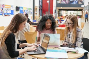 Female Students Working In Communal Area Of Busy College Campus