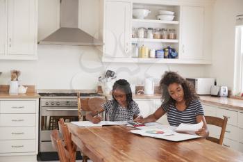 Two Sisters Sitting At Table In Kitchen Doing Homework
