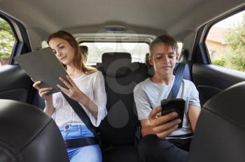 Teenage Children Using Digital Devices On Family Road Trip