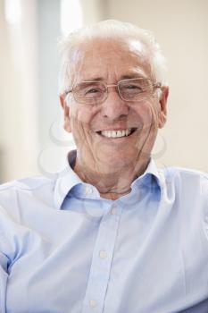 Portrait Of Smiling Senior Man Sitting On Sofa At Home