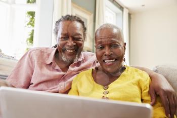 Senior Couple Sitting On Sofa Using Laptop At Home Together