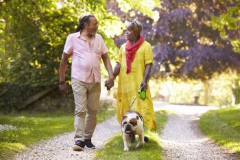 Senior Couple Walking With Pet Bulldog In Countryside