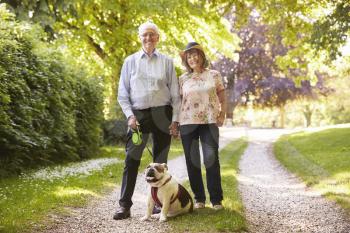 Portrait Of Senior Couple Walking Pet Bulldog In Countryside