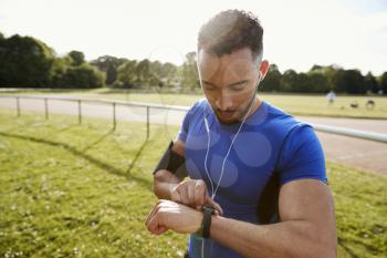 Young man at running track setting fitness app on smartwatch