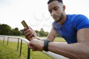 Male athlete using fitness app on smartphone and smartwatch