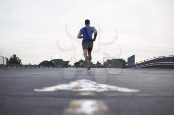 Male athlete running on a road away from camera, full length