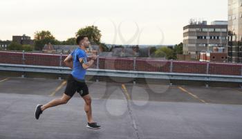 Young male athlete running on a road, side view