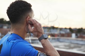 Male runner adjusting earphones in urban setting, close up